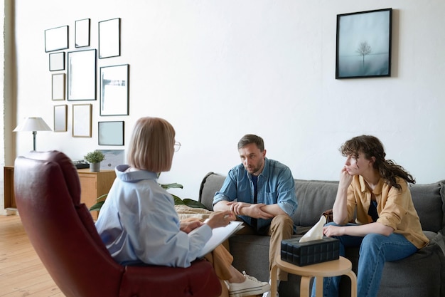 Young couple sitting on sofa at psycho session and listening to recommendations of professional