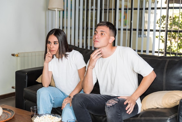 young couple sitting on their couch at home watching a football game