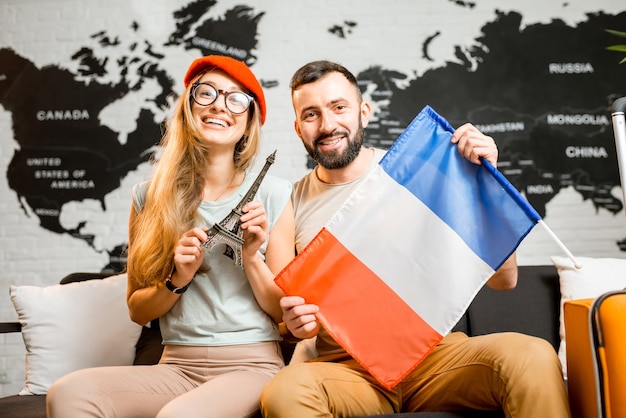 Photo young couple sitting with eiffel tower and french flag at the travel agency office on the world map background prepairing for a trip to paris