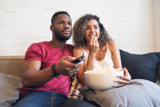 Young couple spending time together and watching tv series or movies while sitting on couch at home.