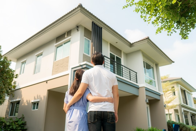 Young couple standing and hugging together looking happy in front of their new house