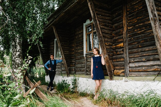 Young couple standing near an old wooden stylish house on the background of birch and nature