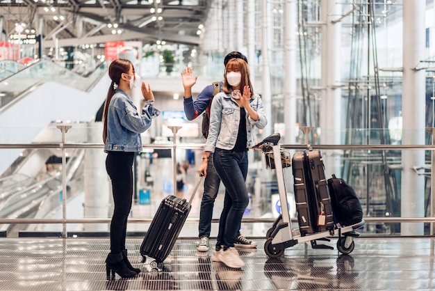 Young couple traveler in quarantine for coronavirus wearing surgical mask face protection waving hi and saying hello with friend after long travel vacation flight at International terminal airport