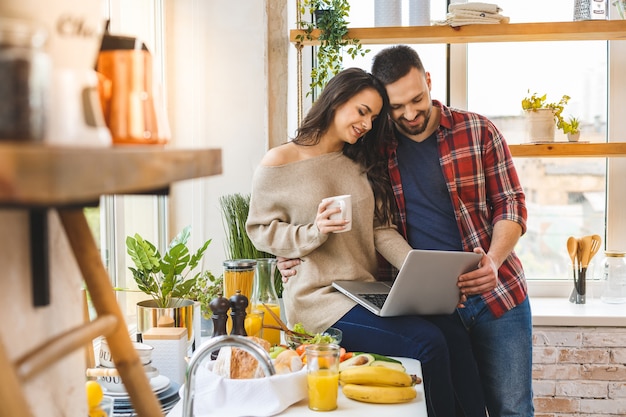 Young couple using laptop to look up recipe for their meal in kitchen.