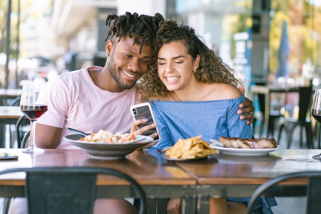 Young couple using a mobile phone and spending good time together while having lunch at a restaurant.