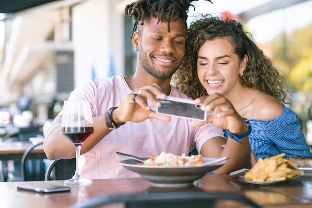 Young couple using a mobile phone and taking photos to the food while having lunch together at a restaurant.