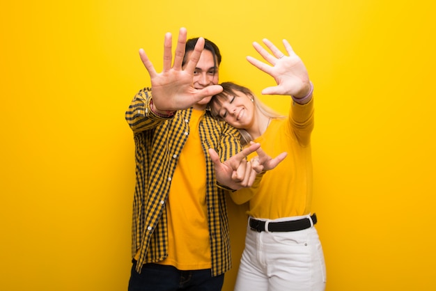  Young couple over vibrant yellow background counting seven with fingers