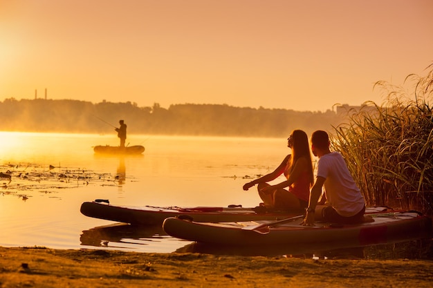 A young couple walks along the river sitting on a sap board and admiring the morning scenery