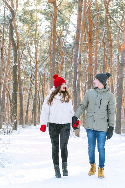 Young couple walks in winter through the forest holds hands and look at each other. Happy lovers walk in snowy park. Vertical frame