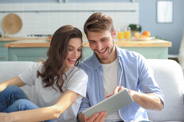 Young couple watching media content online in a tablet sitting on a sofa in the living room.