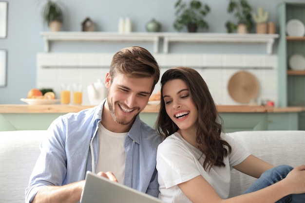 Young couple watching media content online in a tablet sitting on a sofa in the living room.