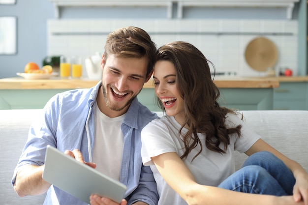 Young couple watching media content online in a tablet sitting on a sofa in the living room.