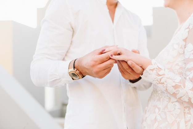 Young couple wearing white wedding dress and shirt, exchanging rings at their dream wedding ceremony