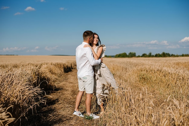 Young couple in the wheat field on sunny summer day. Couple in love have fun in golden field. Romantic couple in casual clothe outdoodrs on boundless field