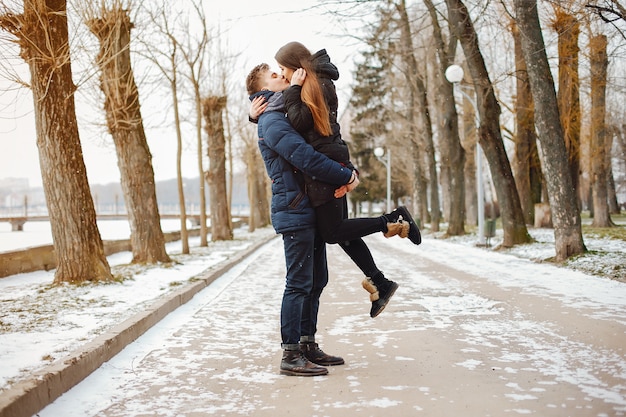 A young couple in winter jackets and scarves walk in a snowy park