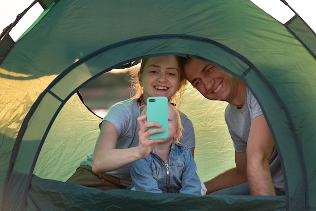 Young couple with child in tourist tent are looking at the phone Holidays with children