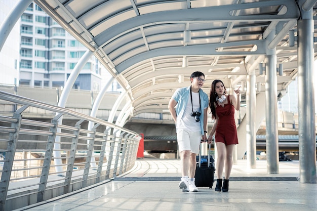 Young couple with dragging a suitcase and talking happily with smiling while to travel in the city. Happiness of young man and young woman in traveling travel together. Travelling concept.