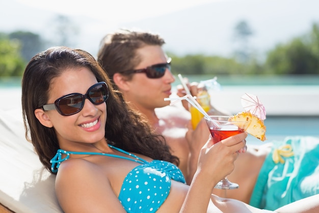 Young couple with drinks by swimming pool