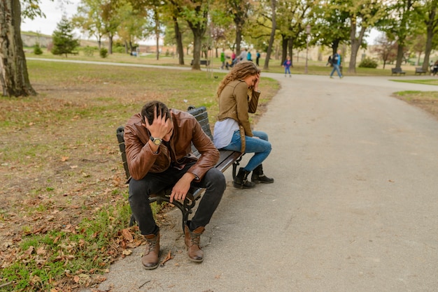 Young couple with the love problems sitting in the city park