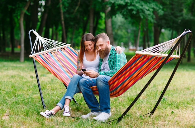 Young couple with mobile phone sitting on hammock