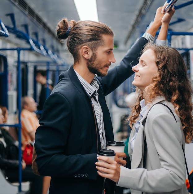 young couple with takeaway coffee standing in subway car