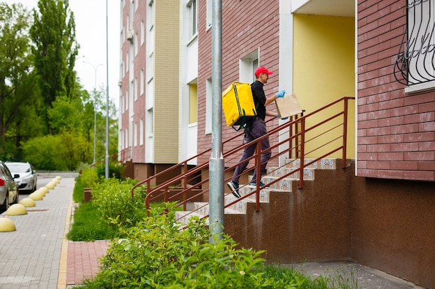 Young courier with thermo bag near the house. Food delivery service