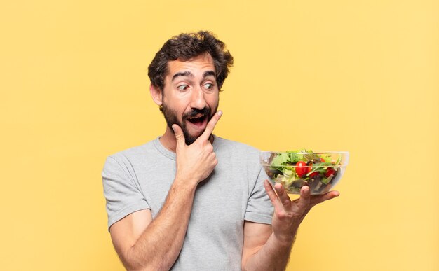 Young crazy bearded man dieting thinking expression and holding a salad