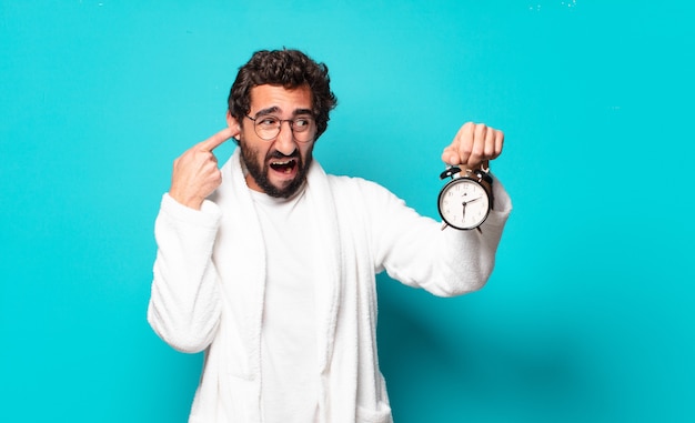 Young crazy bearded man wearing bathrobe and an alarm clock