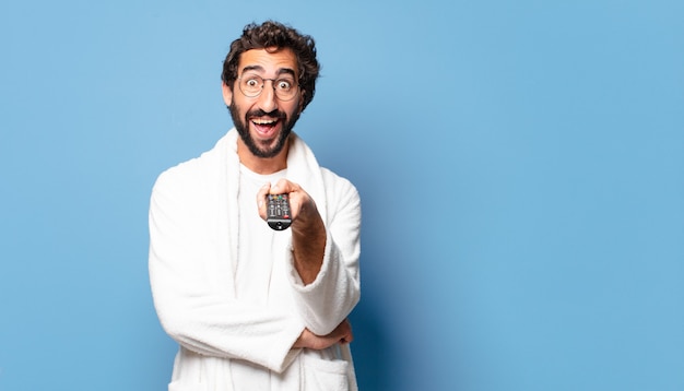 Young crazy bearded man wearing a bathrobe with a remote control