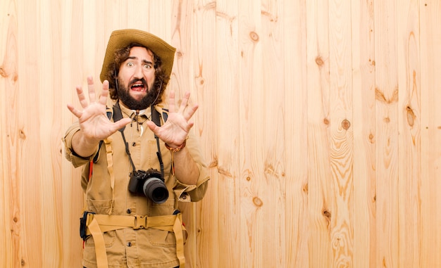 Young crazy explorer with straw hat and backpack on wooden wall 