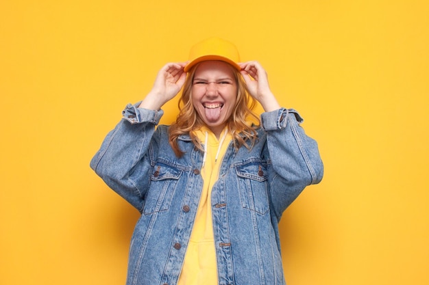 Young crazy girl in denim jacket and cap posing on yellow isolated background