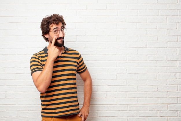 Young crazy or silly man gesturing and expressing emotions against brick wall background