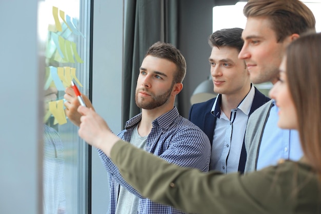 Young creative startup business people on meeting at modern office making plans and projects with post stickers on glass