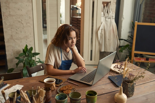 Young creative woman concentrating on network while sitting in workshop