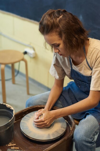 Photo young creative woman sitting by rotating pottery wheel