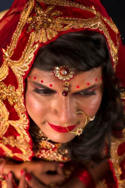 Young crossdresser man wearing Indian wedding clothes of a bride with bridal makeup and posing on grey background looking fashion and glamorous