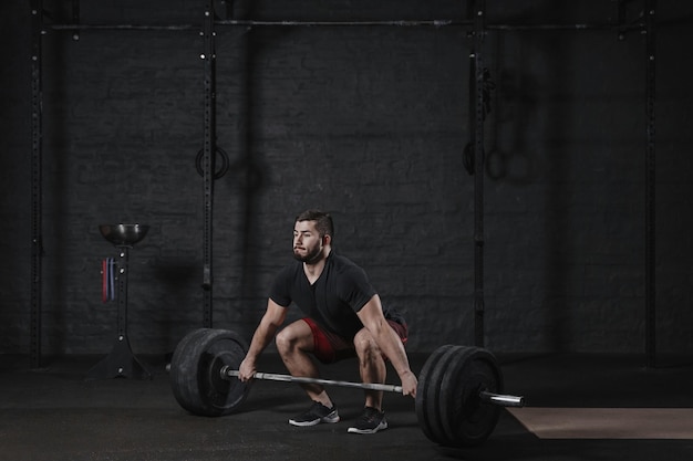 Young crossfit athlete doing deadlift exercise with heavy barbell at the gym Man practicing functional training powerlifting workout