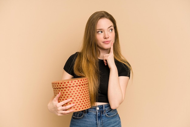 Young, curious Caucasian woman holds a mysterious, closed Valentine's gift, pondering its contents.