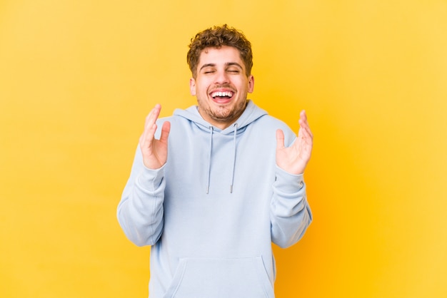 young curly blond man having fun against a yellow wall