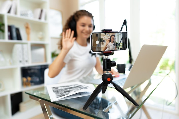 Young curly female blogger recording video at table at home