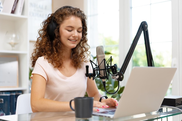 Young curly female recording podcast from home and talking into a microphone