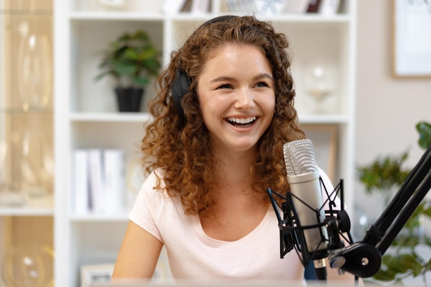 Young curly female recording podcast from home and talking into a microphone