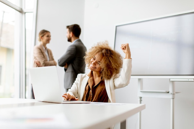 Young curly hair joyful businesswoman using laptop in the office with young people works behind her