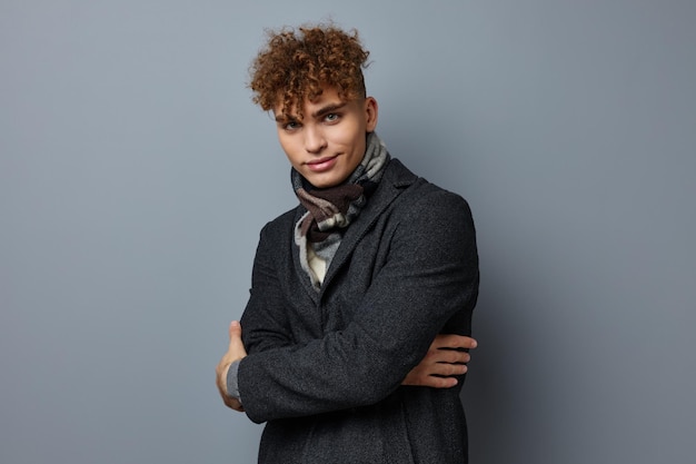 Young curly man in a coat in the studio posing on a gray background