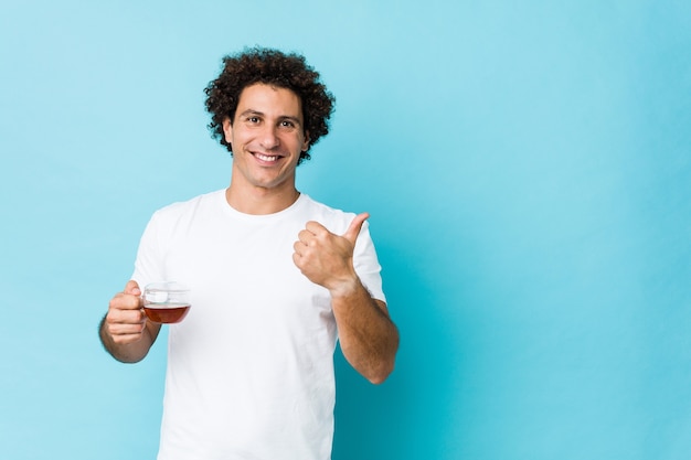 Young curly man holding a tea cup smiling and raising thumb up