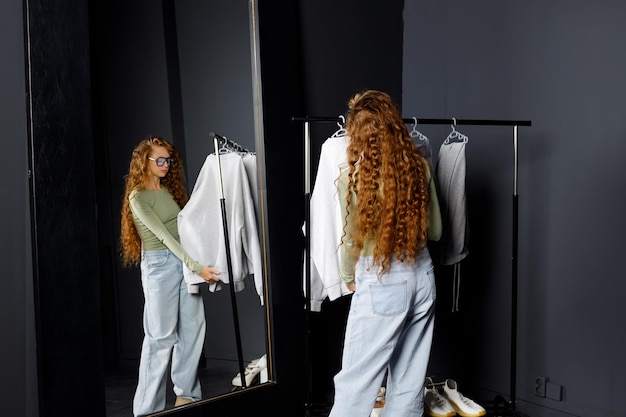 Photo young curly woman choosing clothes at fitting room shopping concept