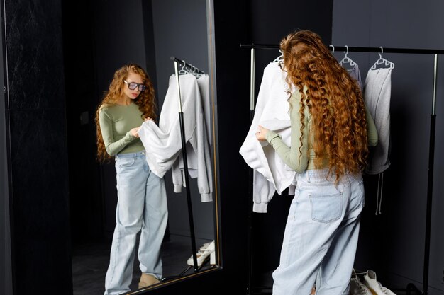 Photo young curly woman choosing clothes at fitting room shopping concept