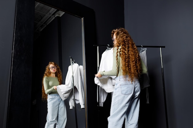 Photo young curly woman choosing clothes at fitting room shopping concept