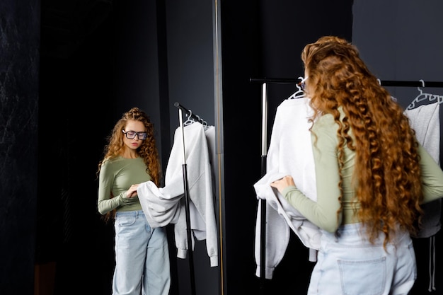 Photo young curly woman choosing clothes at fitting room shopping concept