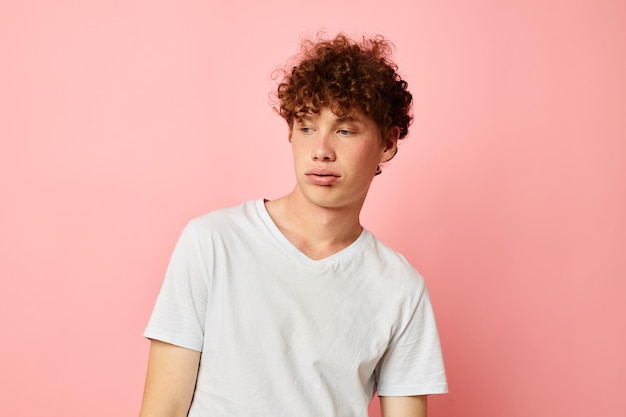 Young curlyhaired man posing youth style white tshirt pink background unaltered